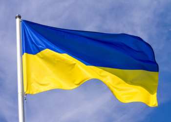 Flag of Ukraine waving in the wind on flagpole against the sky with clouds on sunny day, close-up