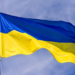 Flag of Ukraine waving in the wind on flagpole against the sky with clouds on sunny day, close-up